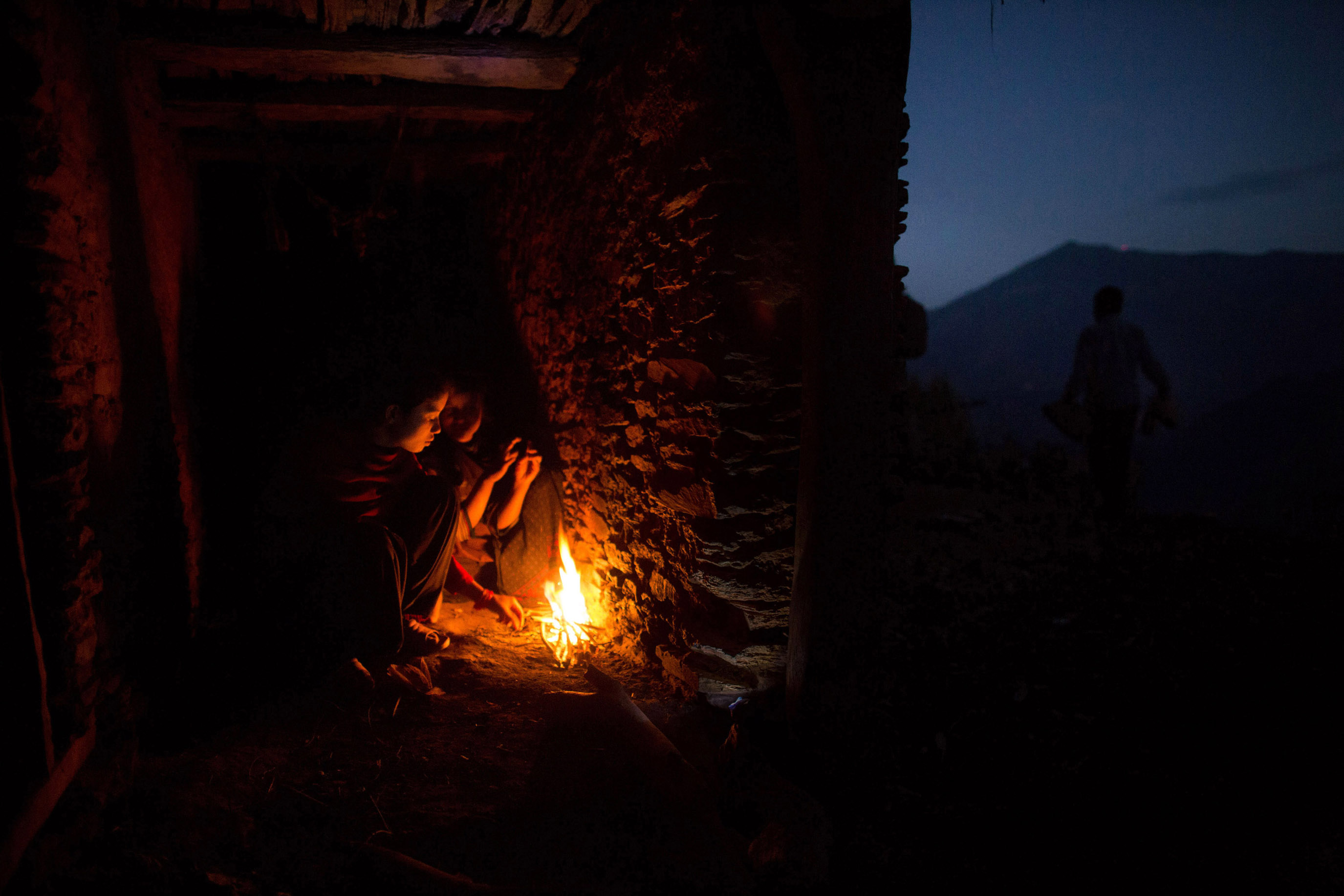 Nabina (left), 17, and Khadi, 12, huddle around a fire for warmth as they prepare to sleep in the household chaupadi shelter, a crawlspace with no door under the home shared with the family's animals.