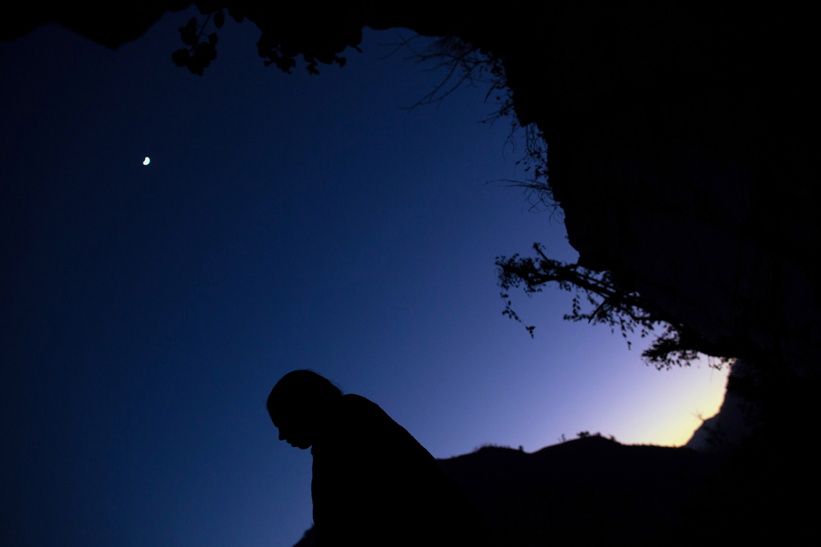 The moon glows overhead as Maisara, 15, prepares to sleep under a rock outcropping in observance of chaupadi in Kalekanda village.