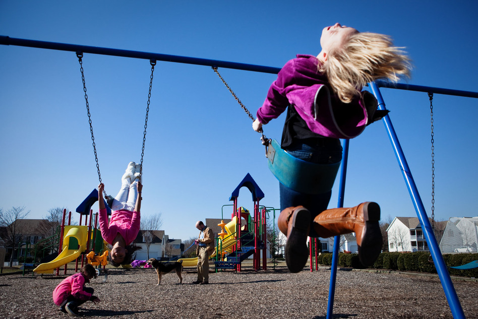Brown checks his phone while his daughters Anita and Anna play on a swing set near their home.