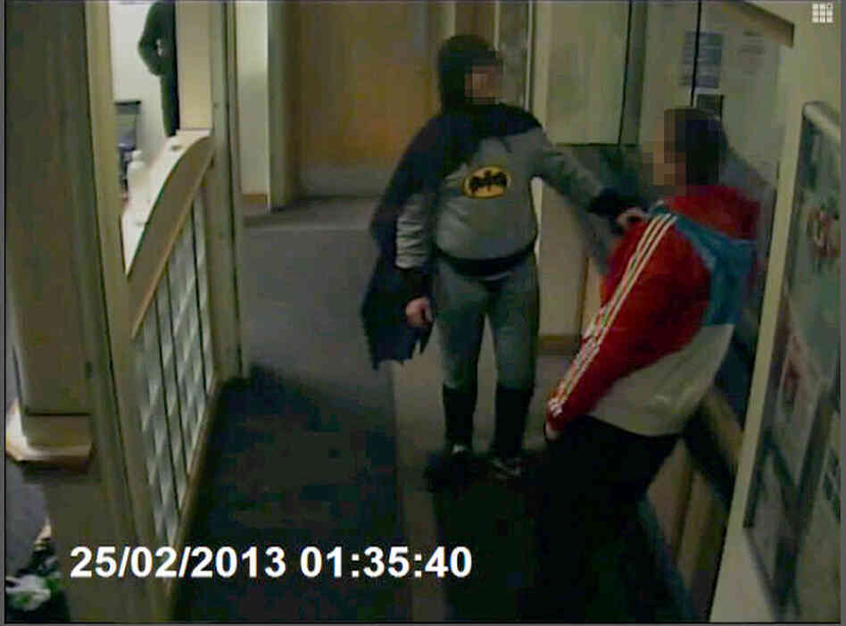 Batman brings in a wanted man to a police department in England. Batman brings in a wanted man to a police department in England.
