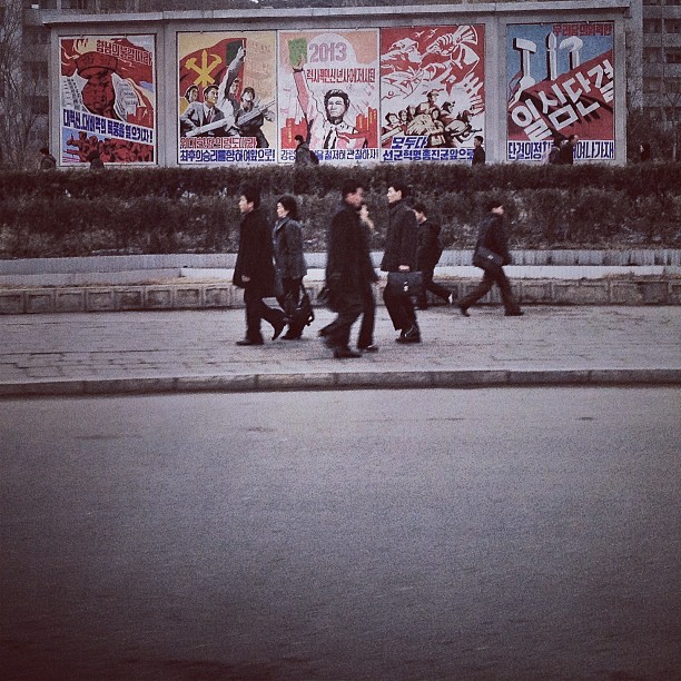 "North Korean commuters pass by propaganda posters in #Pyongyang."