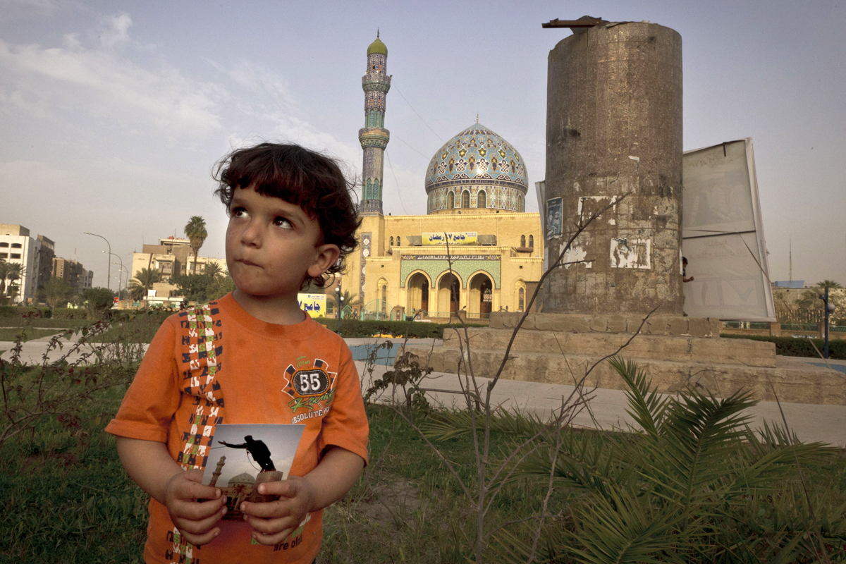 Hussein, 3, poses in Firdous Square in Baghdad with a 2003 photograph taken by Jerome Delay — showing the statue of Saddam Hussein being pulled down by U.S. forces and Iraqis.