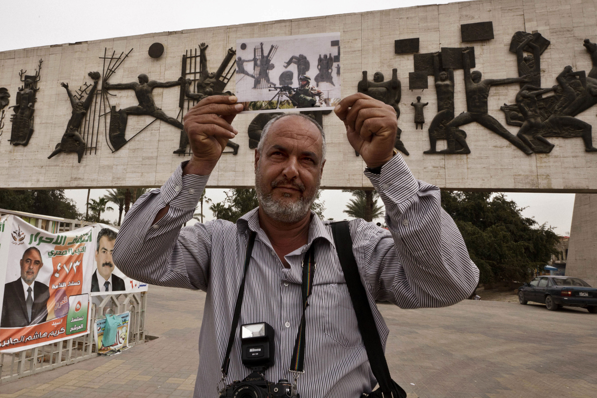 Street photographer Raad Mohammed poses with a photograph taken by photographer Khalid Mohammed in Baghdad's Tahrir Square. The 2006 image shows an Iraqi soldier manning a checkpoint. It was taken after Baghdad was subjected to a vehicle ban — an effort to prevent reprisal attacks from suicide car bombs after the killing of Abu Musab al-Zarqawi.