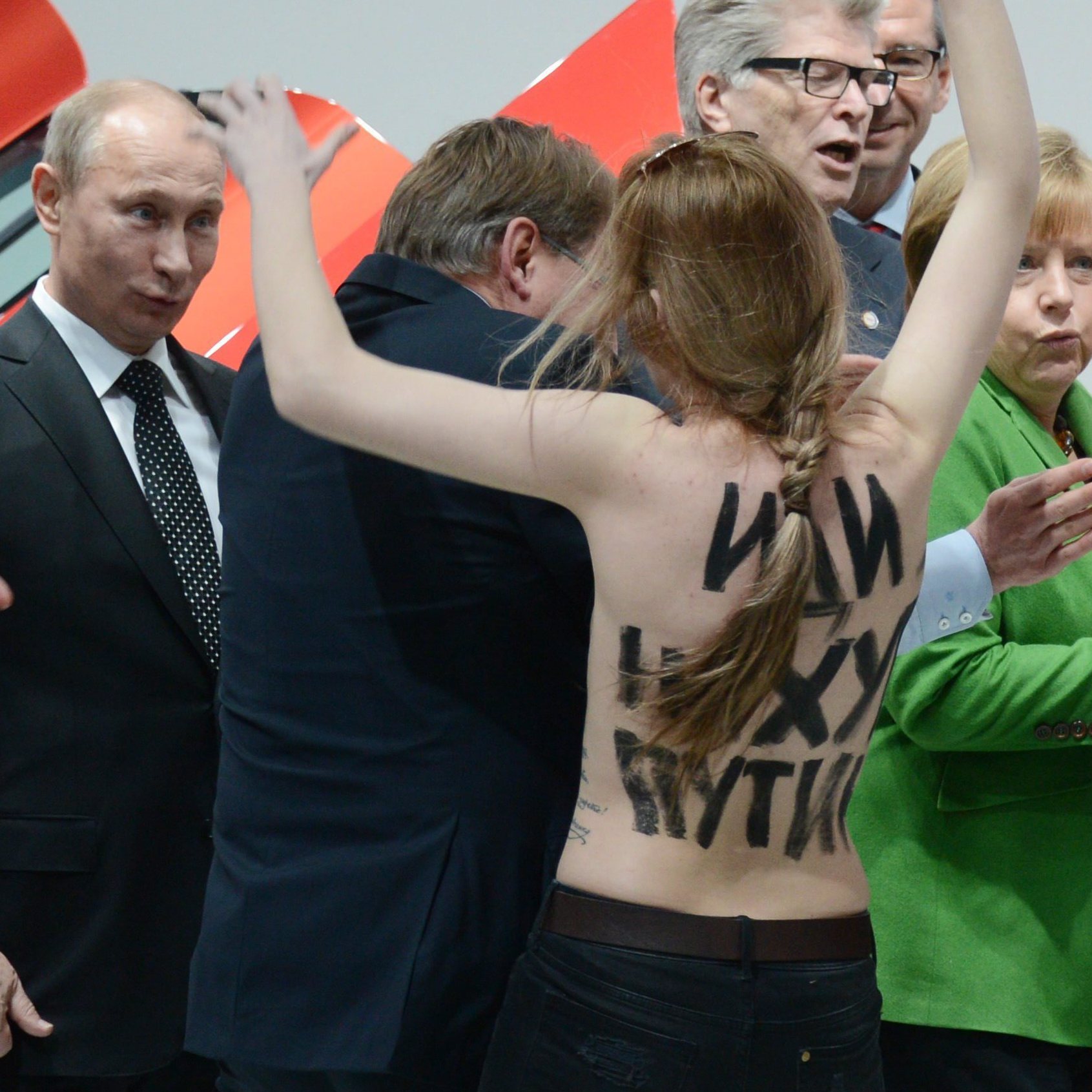 Russian President Vladimir Putin (far left) looks on Monday in Hanover, Germany, as one of three women who stripped off their tops protests his appearance at a trade fair. German Chancellor Angela Merkel is in the green jacket.