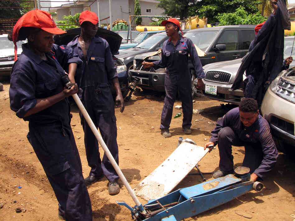 Trainees wear navy overalls, hard boots and tuck their hair into customized caps while working on cars at the Lady Mechanic Initiative. Trainees wear navy overalls, hard boots and tuck their hair into customized caps while working on cars at the Lady Mechanic Initiative.