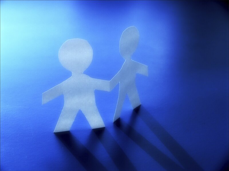Paper cutouts of two figures holding hands on a blue background.