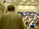 A man stands in front of a crowd in a lecture hall. A man stands in front of a crowd in a lecture hall.