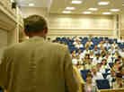 A man stands in front of a crowd in a lecture hall. A man stands in front of a crowd in a lecture hall.