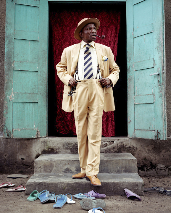 Severin Mouyengo, who has been a <em>sapeur</em> since the 1970s, poses in the entrance of his family house in the Bacongo neighborhood. Sandals on the ground are from his family members.