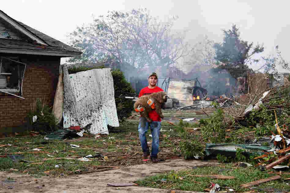 A neighbor carries a soggy, shivering dog away from a pile of rubble in Moore.