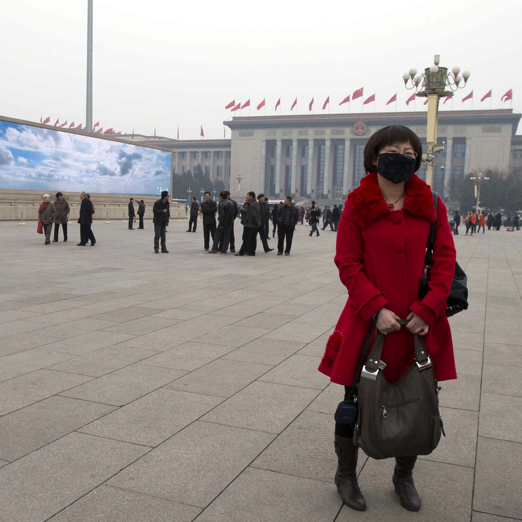 A woman wears a mask as she stands near a giant display depicting blue skies during a day of heavy pollution on Tiananmen Square in Beijing on March 6.