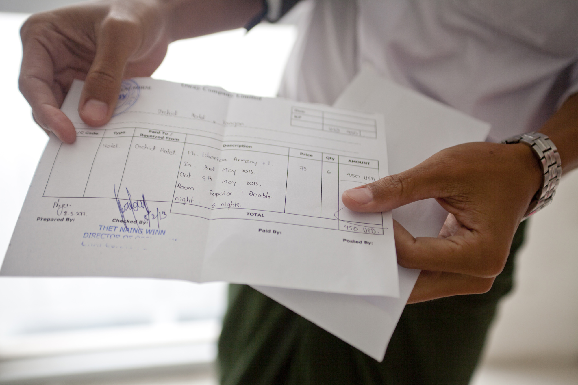 One of Aung's employees holds up the receipt of a payment he is about to deliver to one of Aung's partner hotels. Even though Aung enables tourists to handle their travel bookings online, he still has to deliver cash to his partners by hand.