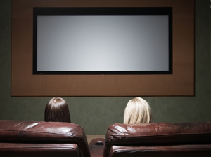 Two women watch a movie screen.