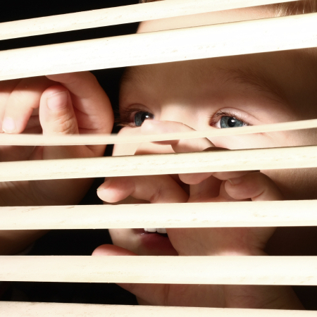 Boy looking through window blinds