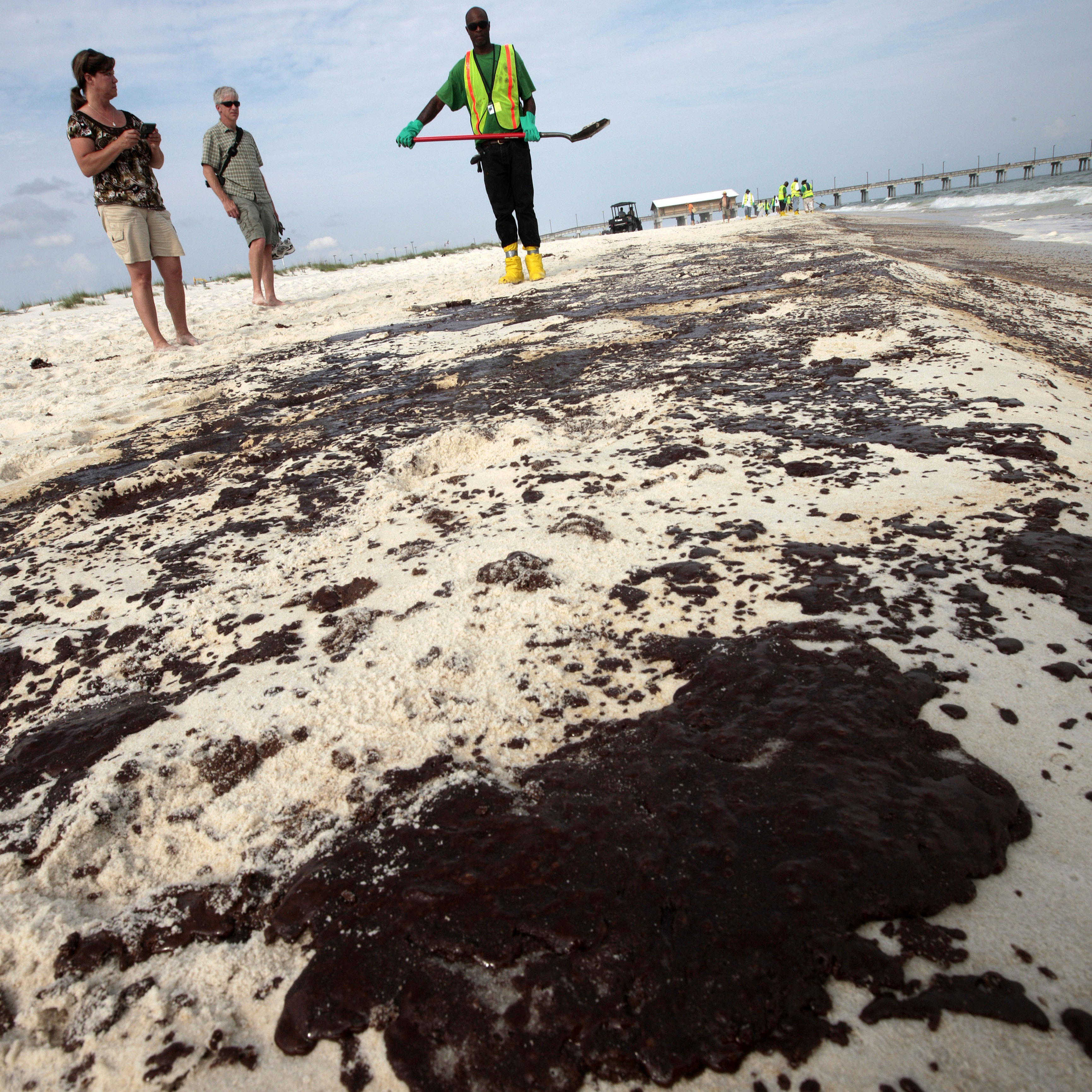 Tourists watch as workers clean oil from the sand along a strip of oil that washed up on the beach in Gulf Shores, Ala., in 2010 after the Deepwater Horizon oil rig exploded off the Louisiana coast.