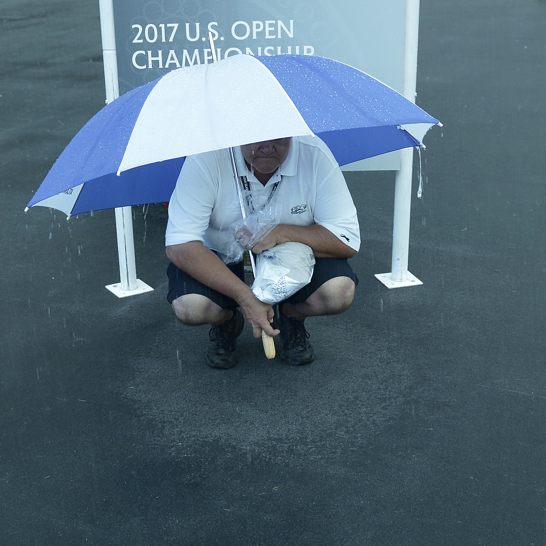 A man finds some shelter from the rain Thursday at the U.S. Open, which is being played at Merion Golf Club in Ardmore, Pa.