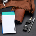 Personal organizer with blank lined page propped against various items spilling out of a brown leather purse. Studio isolated on a black textured background. Personal organizer with blank lined page propped against various items spilling out of a brown leather purse. Studio isolated on a black textured background.