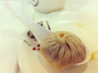 A xiao long bao, or soup dumpling, in a large spoon. A xiao long bao, or soup dumpling, in a large spoon.