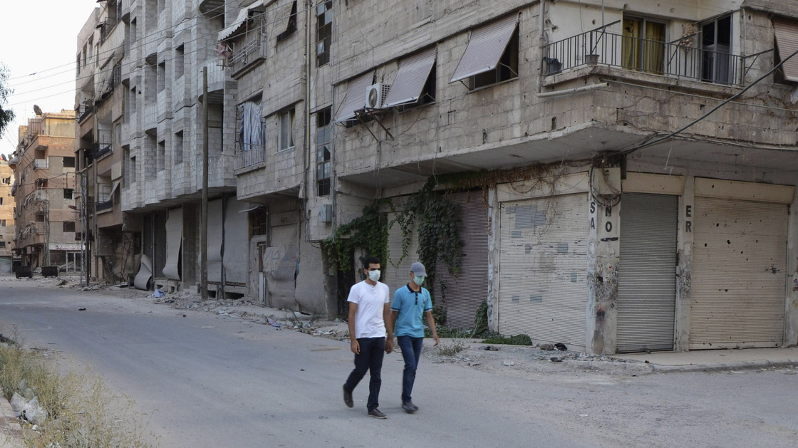 Men wearing masks walk along a deserted street that was hit by what activists said was a gas attack in the Damascus suburb of Ain Tarma on Wednesday.