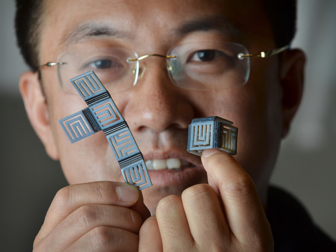 H. Jerry Qi, associate professor of mechanical engineering at Colorado University, holds simple models printed using polymers that have "shape memory." The flat piece on the left can reshape itself into a box with the application of heat.