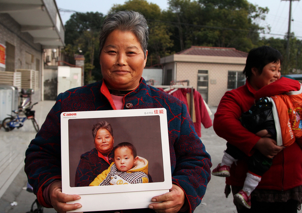 Zheng Jinrong poses with a portrait of herself and her grandson in a migrant village in Shanghai. She received the photographs as part of a global event to provide high-quality portraits for people who otherwise can't afford them. (Image credit: NPR)