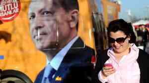A woman looks at her smartphone as she walks by a banner of Turkish prime minister Recep Tayyip Erdogan, in Istanbul on March 21. On Thursday, Turkish court orders banned Internet users from accessing Twitter, but the social media company posted instructions on how to tweet from a phone.