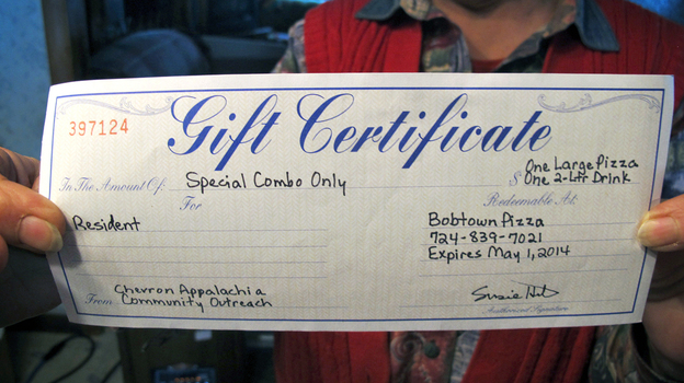 Joann Herrington holds up the gift certificate to Bobtown Pizza that she and her husband received from Chevron three days after a natural gas well exploded up the hill from their home in Mount Morris, Pa. (Image credit: WHYY)