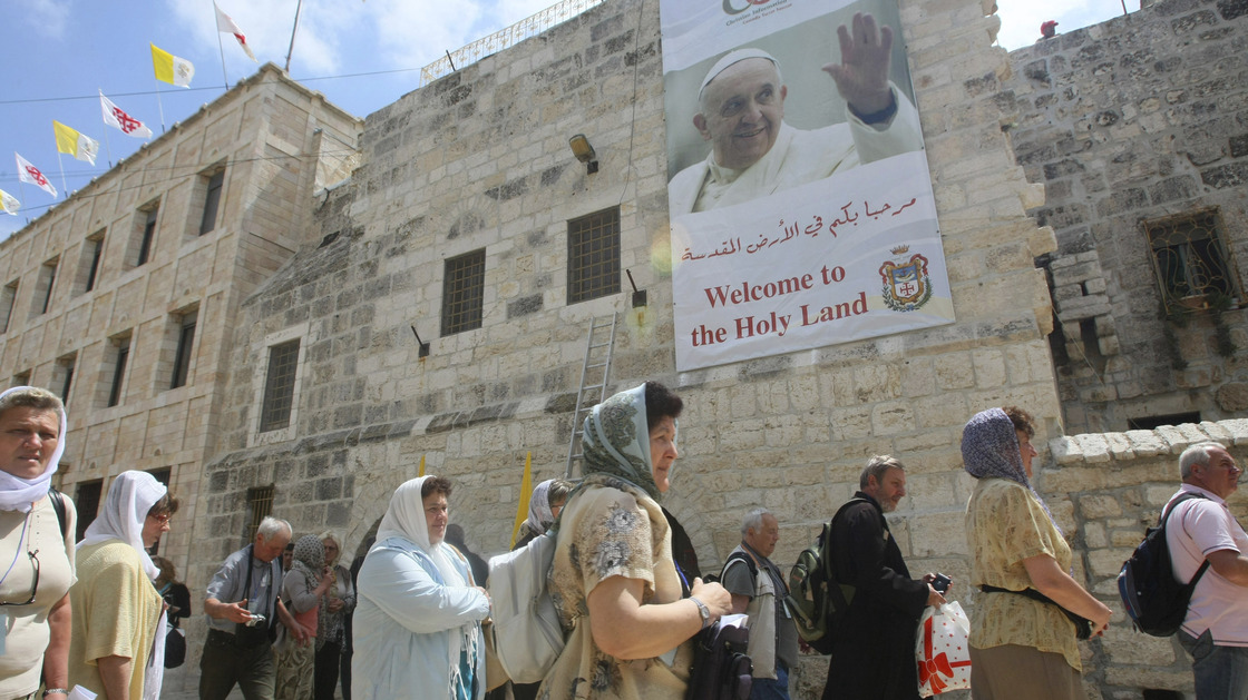 Tourists walk past a poster of Pope Francis hanging on the Church of the Nativity in the West Bank town of Bethlehem on Monday. Pope Francis' trip to the Mideast later this week will commemorate the 50th anniversary of a historic rapprochement between Catholics and Orthodox, who split nearly 1,000 years ago.