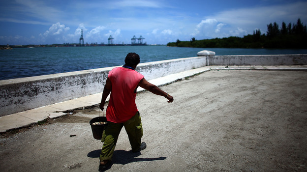 A fisherman walks the streets of Mariel, on Cuba's northeast coast. In the distance, construction is underway on the Port of Mariel, where the government is creating a special free-trade zone. (Image credit: NPR)