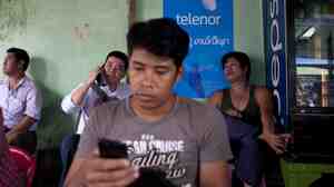 A man uses a mobile phone in front of a Telenor ad for cheap sim cards in Yangon, Myanmar. Cheap mobile technology has ignited an Internet revolution in the once-isolated nation.
