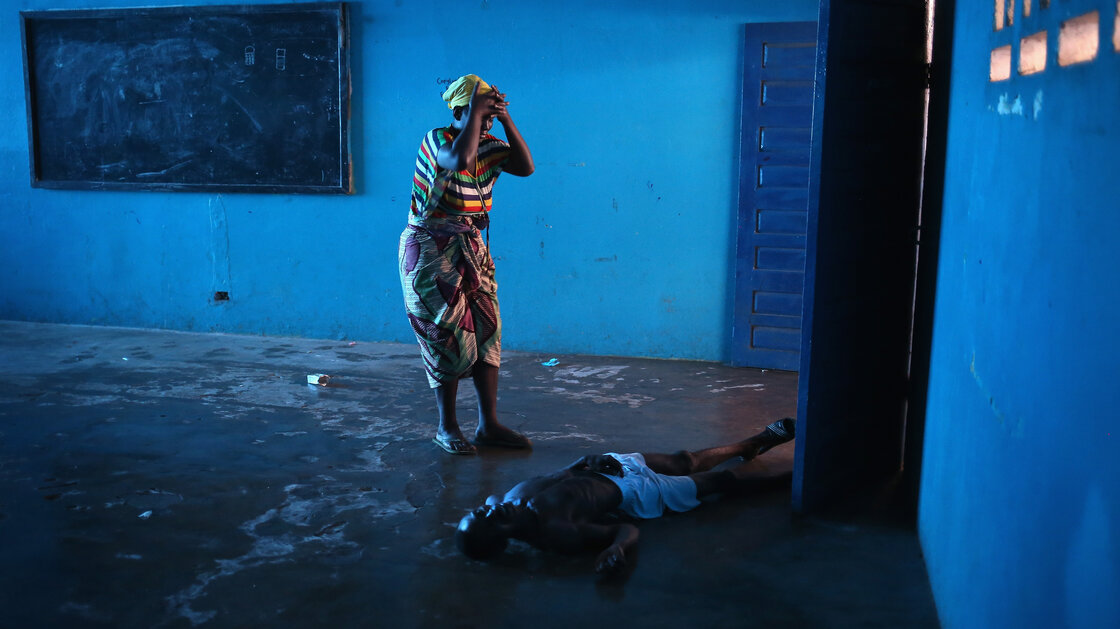 Umu Fambulle stands over her husband, Ibrahim, who'd fallen and knocked himself unconscious in an Ebola ward in Monrovia, Liberia.