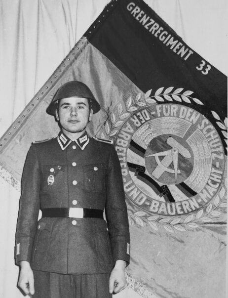 Harald Jaeger in uniform next to the flag of his East German border regiment in 1964.