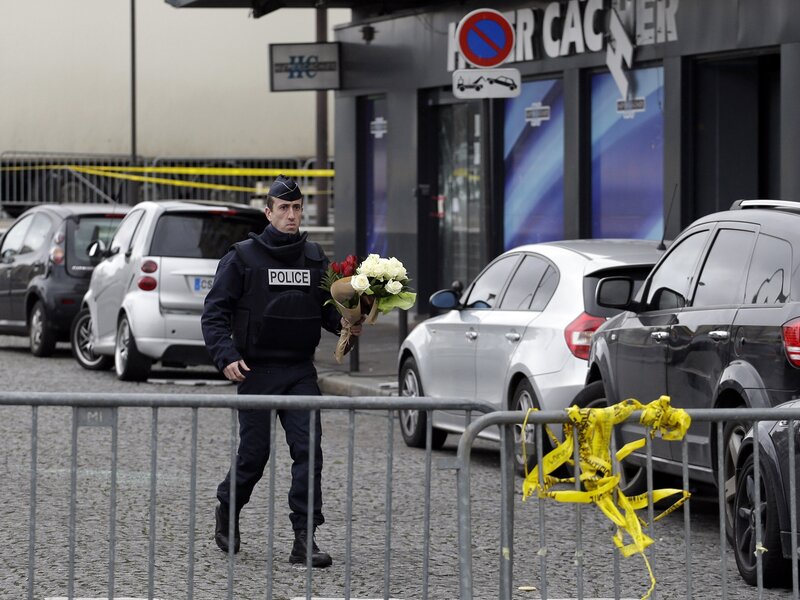 A police officer carries flower tributes at the site of Friday's attack on a kosher market in Paris, France.