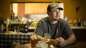 John Coffell sits at his grandmother's table in Hulen, Okla. After he hurt his back at a tire plant last year, his wages dropped so dramatically that he and his family were evicted from their home.