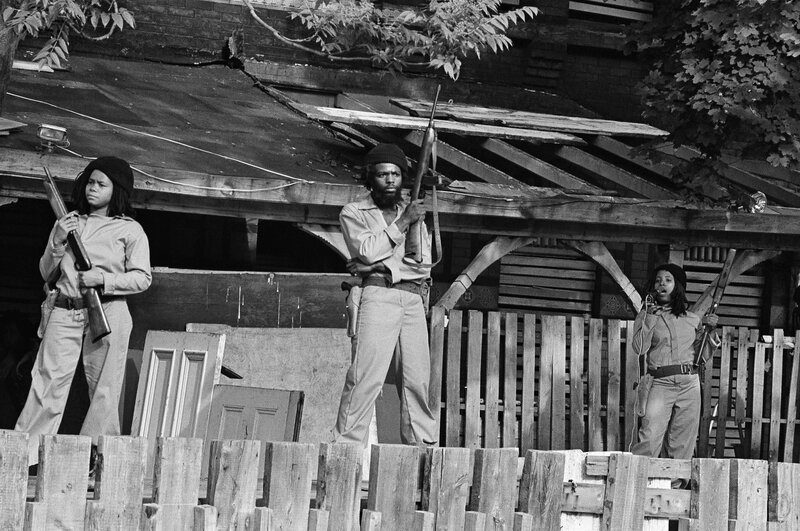 MOVE members hold sawed-off shotguns and automatic weapons as they stand in front of their barricaded headquarters on May 21, 1977.