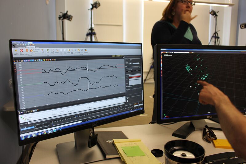 Jason Lamberton, ML2's tech consultant, points to the motion capture marker's position on screen. The left screen displays a graph featuring the temporal rhythms of a simple nursery rhyme suited for a 6- to 18-month-old: a boat on a wave.