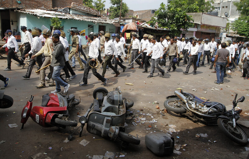 Indian policemen in plain clothes walk past vehicles damaged during a clash between two groups in Ahmadabad, India, Tuesday, Aug. 25, 2015. Clashes were reported in parts of the city after tens of thousands of members Gujarat's Patel community held a rally demanding affirmative action for better access to education and employment. (Ajit Solanki/AP)