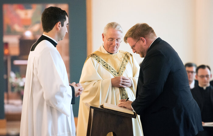 The Rev. Phillip Brown, center, watches as Tom Lawrence, right, a first-year pre-theologian at Theological College, signs the Book of Inscription during the school's opening Mass in August. (Courtesy of The Catholic University of America)