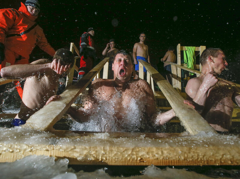 Russian Orthodox believers swim in frigid water at a pond outside St. Petersburg in the wee hours of Tuesday morning. Warmly dressed emergency medical technicians stand by in case anyone is overcome by the cold.