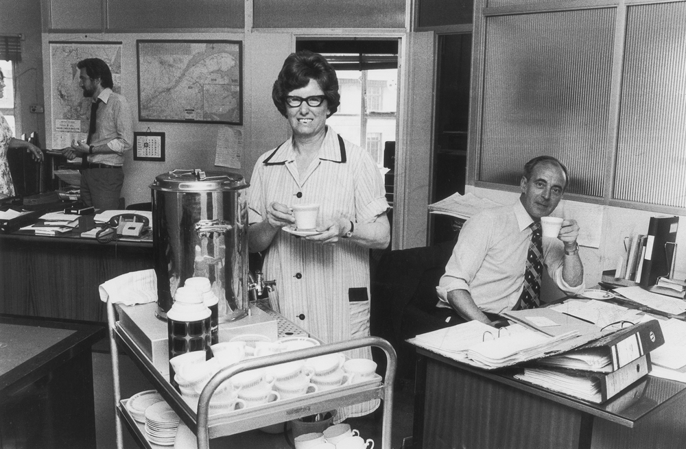 A tea lady brings round refreshments for British office workers in the 1970s. All over the U.K., the arrival of the tea ladies with trolleys loaded with a steaming tea urn and a tray of cakes or buns was the high point of the workday.