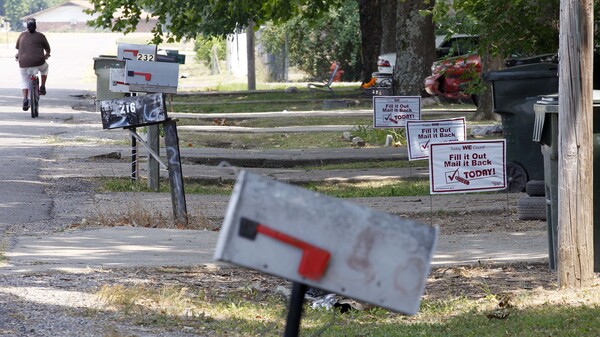 A bicyclist pedals past signs promoting the 2010 census outside homes in Rolling Fork, Miss., in 2010.