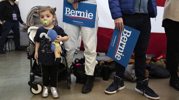 Goldie Federico-Rubin, 2, of Des Moines, stands next to her mom, Laura Federico, as they list to Democratic presidential candidate Sen. Bernie Sanders (I-Vt.) Saturday, Jan 11, 2020 during a campaign event at Berg Middle School in Newton, Iowa.