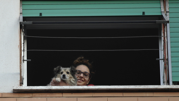 A girl and her dog look out from a window during one of the many flash mobs taking place in Rome, on Sunday. The nationwide lockdown to slow coronavirus is still in its early days for much of Italy, but Italians are already showing signs of solidarity.