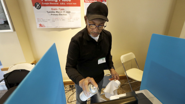 John Davis, a polling judge volunteer, sanitizes an electronic voting machine screen amid concerns about the COVID-19 coronavirus at a polling place in the Bronzeville neighborhood of Chicago, Tuesday, March 17.