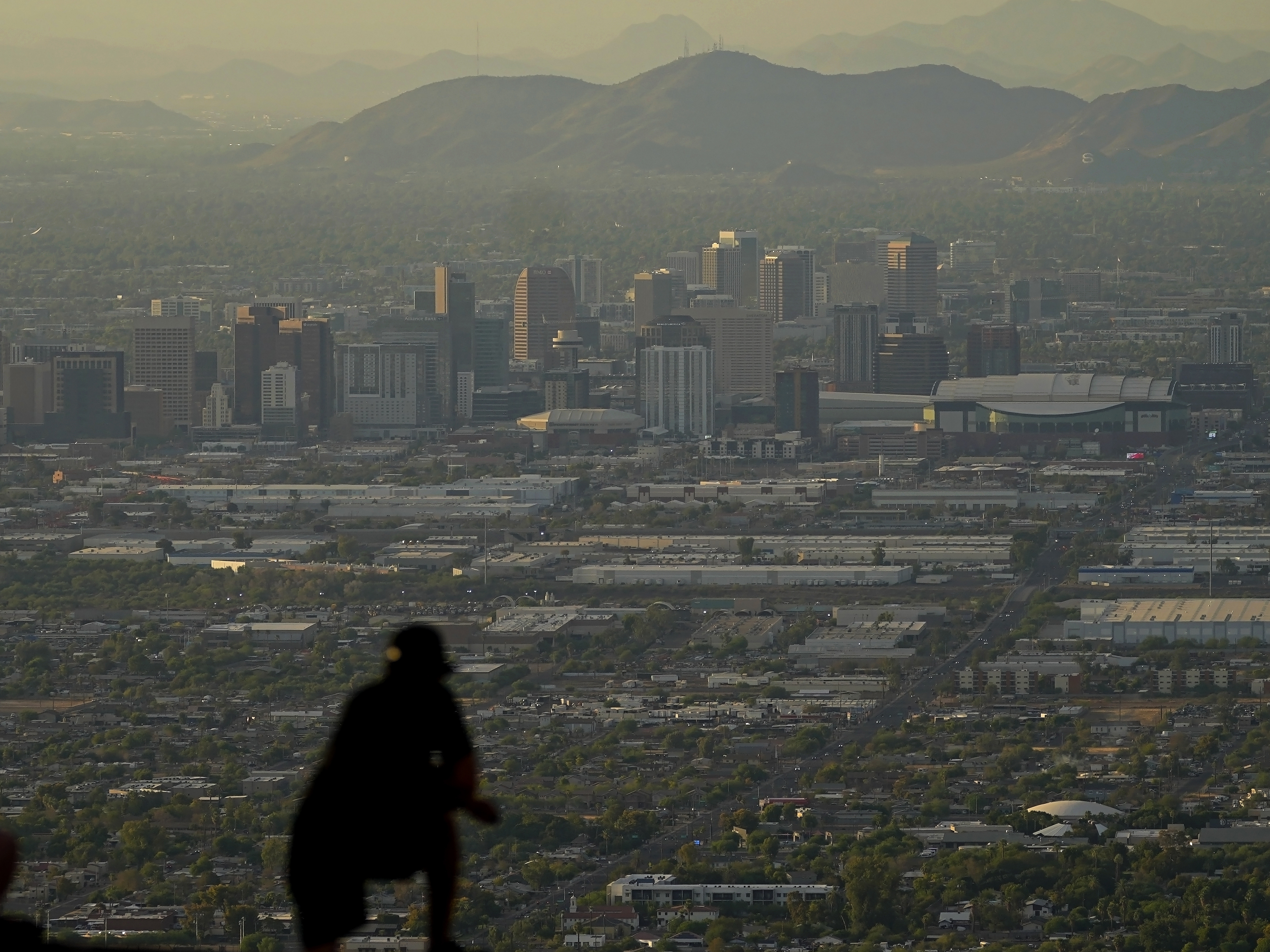 A man overlooks downtown Phoenix at sunset atop South Mountain on Sunday. Some slight relief may be on the way as seasonal thunderstorms could drop temperatures in Phoenix on Tuesday.
