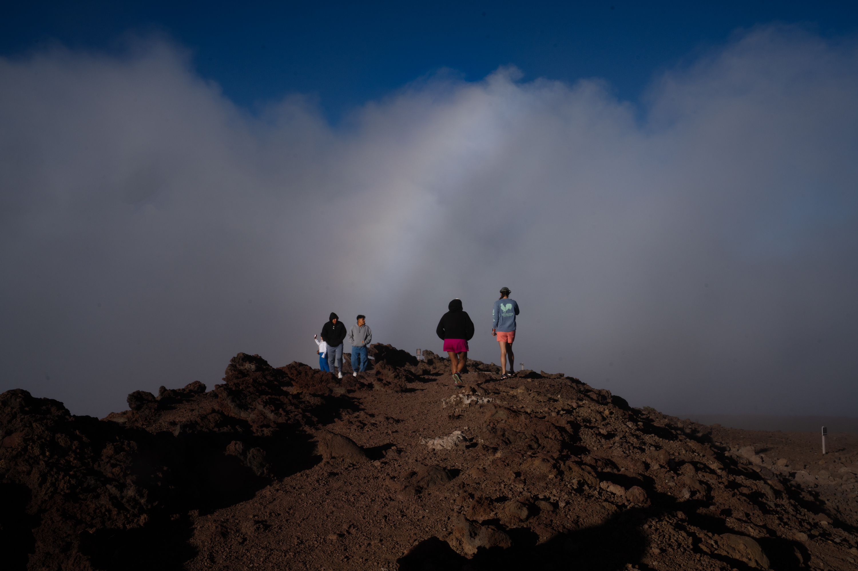 A few tourists stand under a rainbow as the clouds clear at Haleakalā on the island of Maui, Hawaii. Though much of the island is untouched, tourism is down drastically.