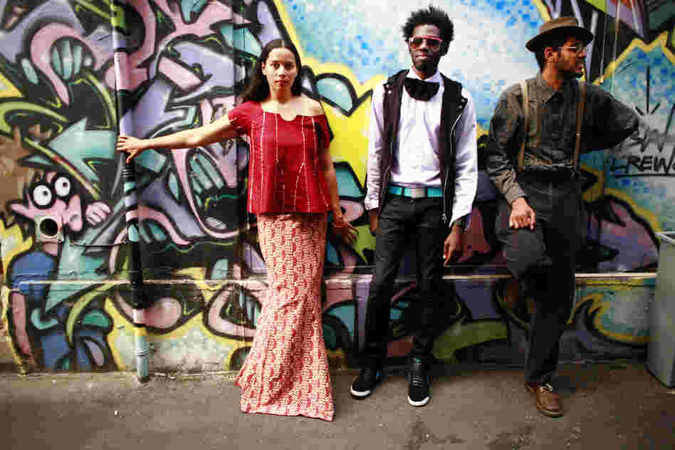 The three members of Carolina Chocolate Drops stand in front of a mural