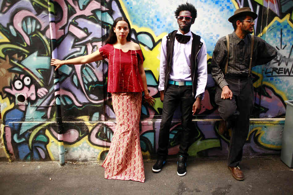 The three members of Carolina Chocolate Drops stand in front of a mural