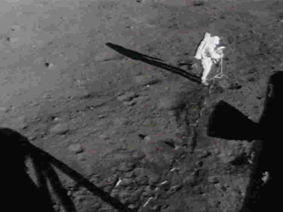 Astronauts move the lunar camera onto a tripod on the moon.