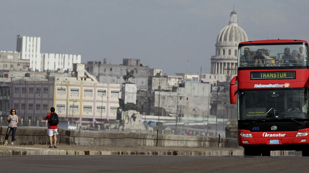 Tourists take photos as a sightseeing bus drives by along Havana's Malecon